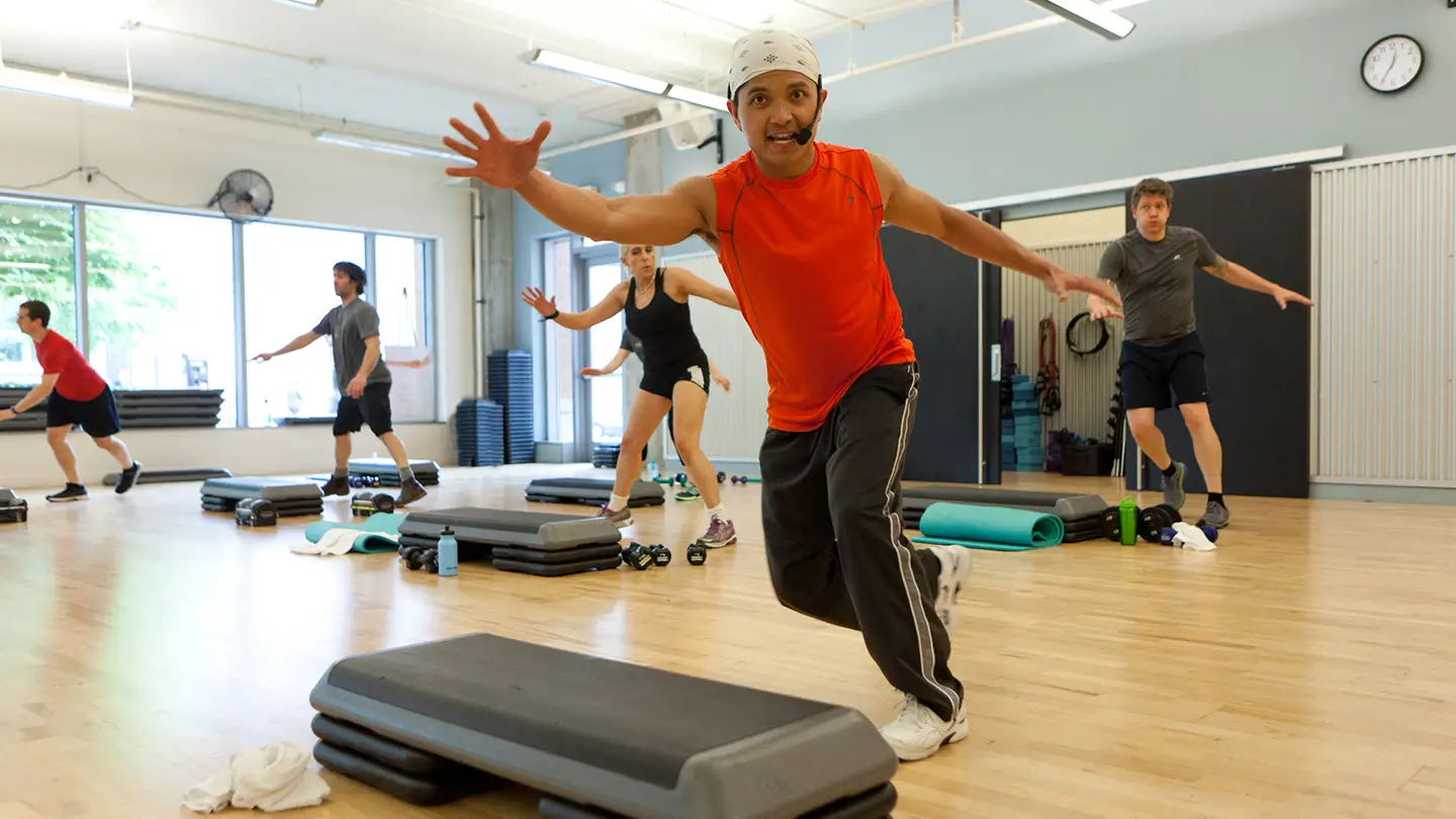 A man wearing a white hat and orange shirt is running on a treadmill.