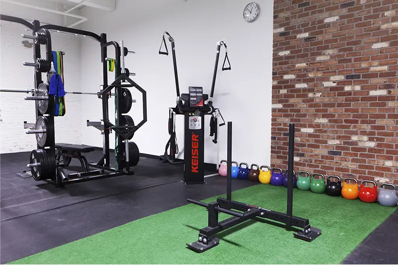 A black and green gym equipment with a clock on the wall.
