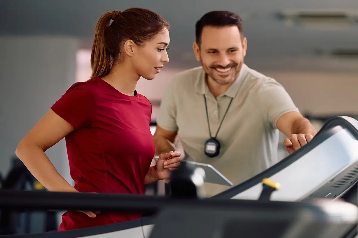 A woman wearing a red shirt and a man wearing a white shirt are standing in front of a computer.