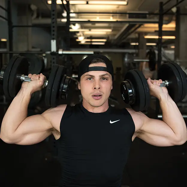 A man wearing a black shirt and a black hat lifting weights in a gym.