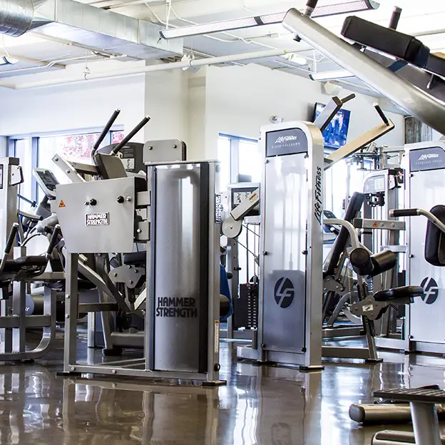 A gym with a variety of machines and a large mirror.