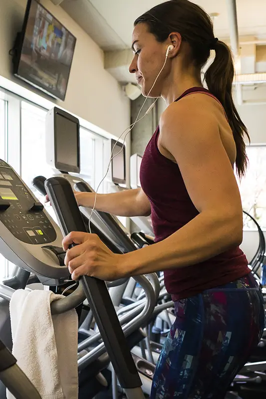 A woman wearing headphones and a red shirt is on a treadmill.