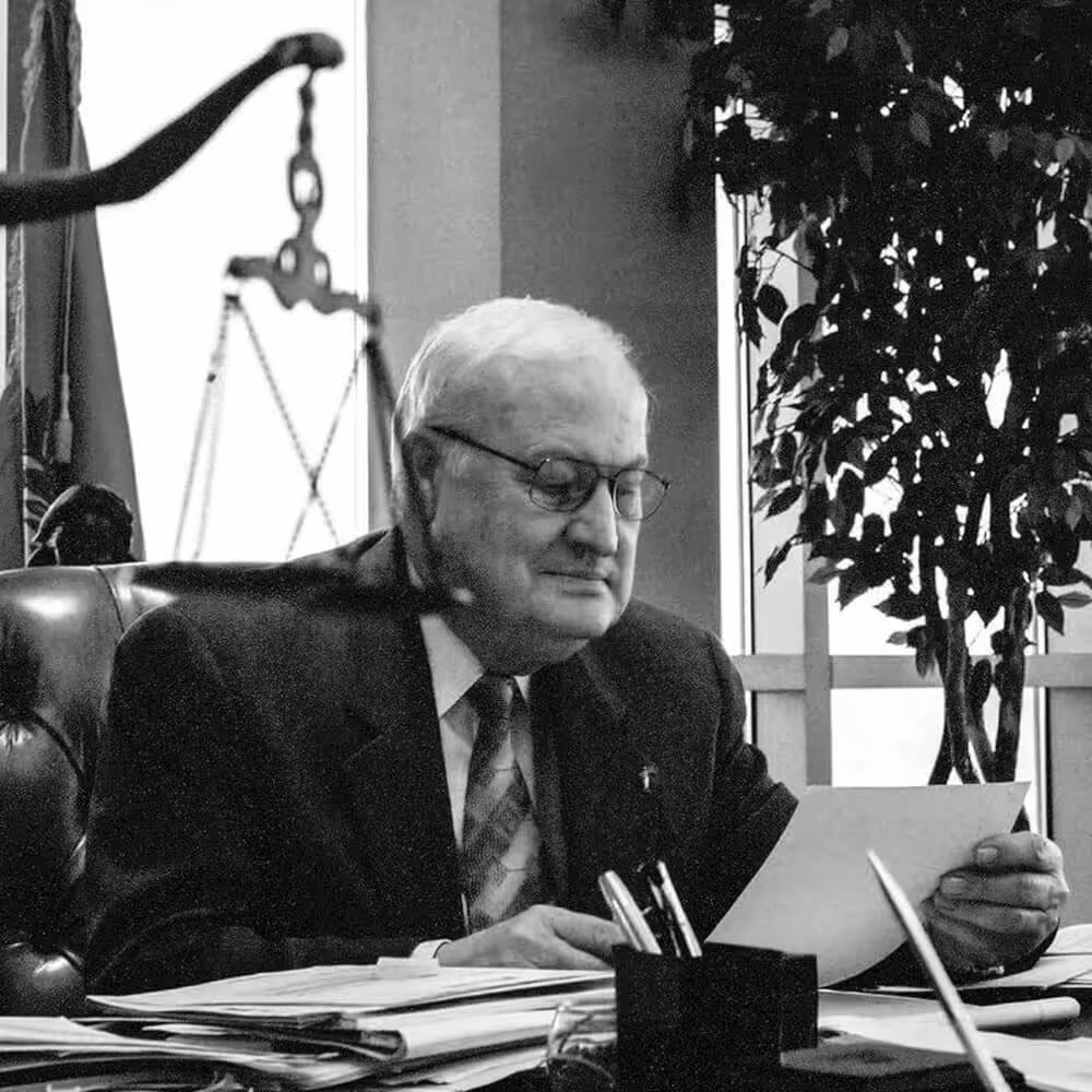 Black-and-white portrait of Harland Stonecipher seated at a desk reviewing documents.