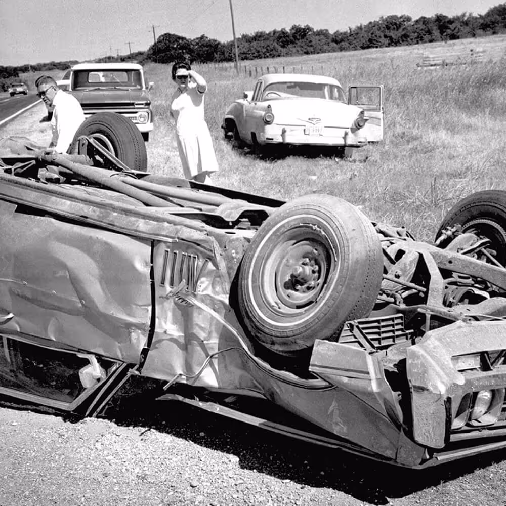 Historic black-and-white photo of an overturned car on the roadside, representing the company’s origins in legal protection after an auto accident.