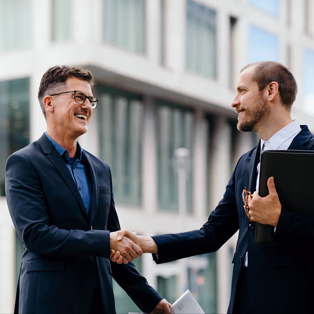Two business professionals shaking hands outside an office building, representing business trial defense support and legal representation.