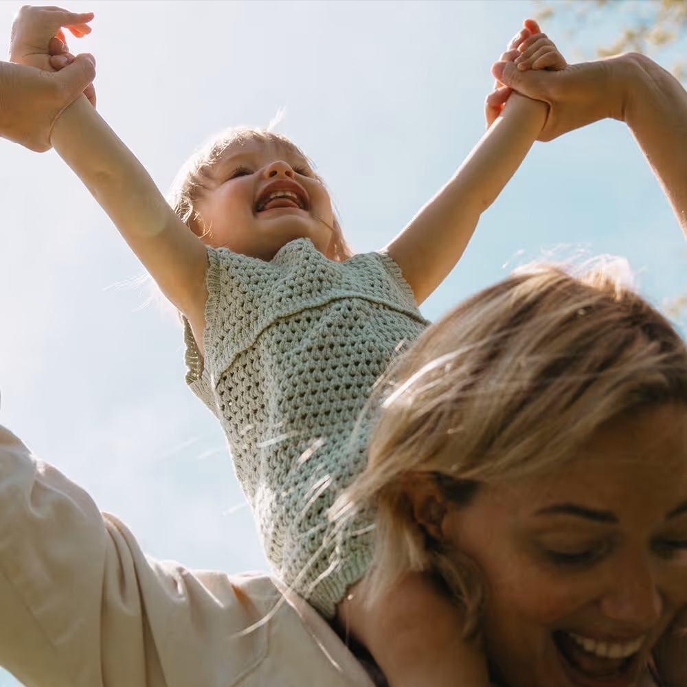 Child smiling while being lifted by adults outdoors, representing family-focused personal legal protection.