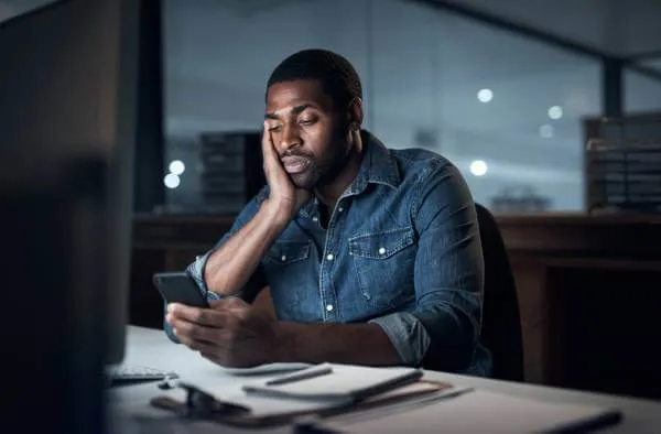 stressed employee working at his desk late looking at his phone