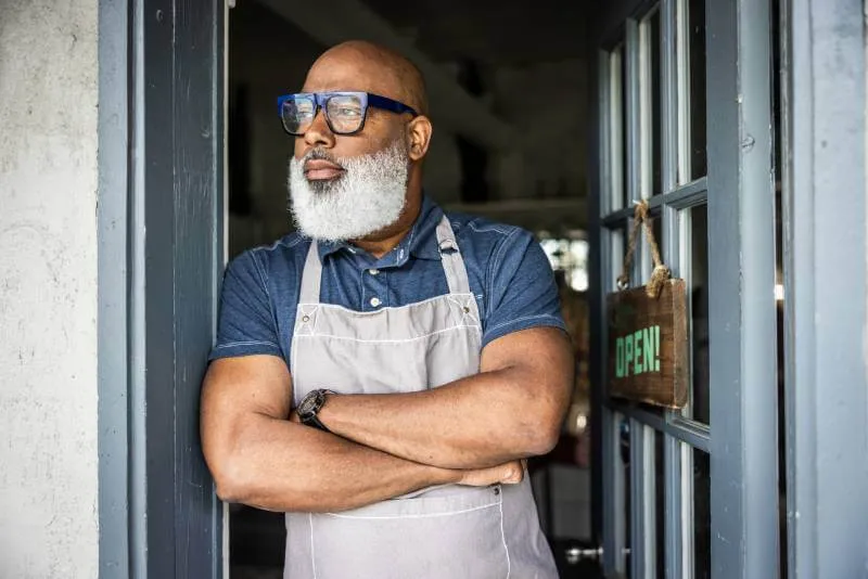 Small business owner standing in the doorway of his business contemplating selling his business