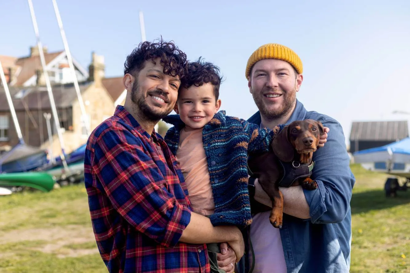 same-sex couple and their young son and dog standing outside by boats