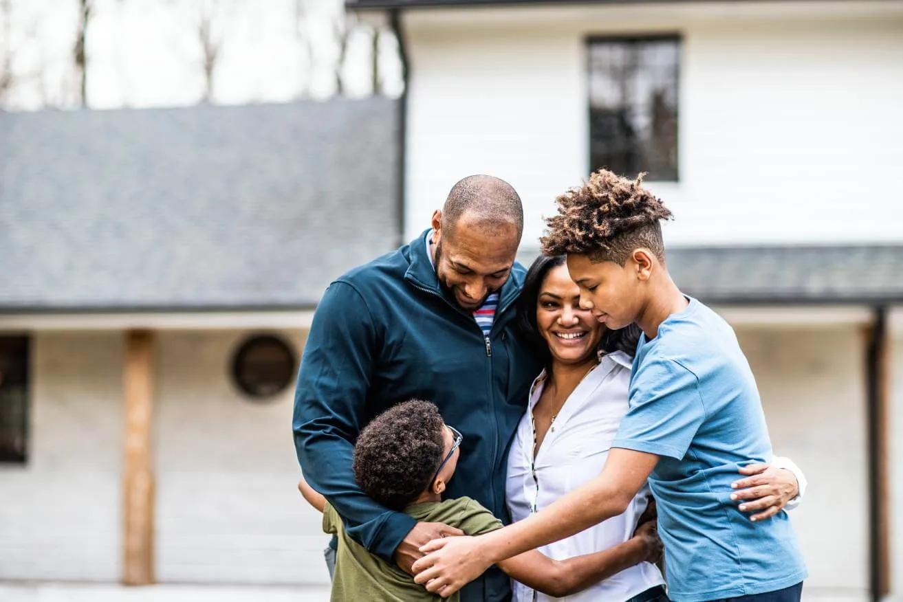 family of four embracing in yard in front of home