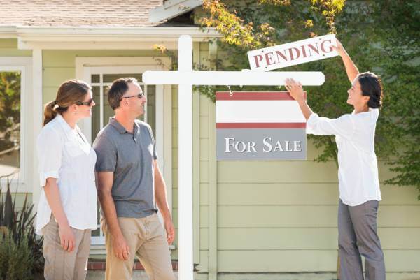 pending sign being added to a home for sale sign my a real estate agent as the home sellers look on