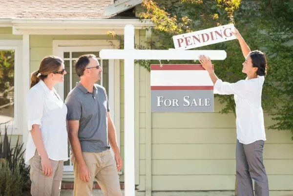 pending sign being added to a home for sale sign my a real estate agent as the home sellers look on