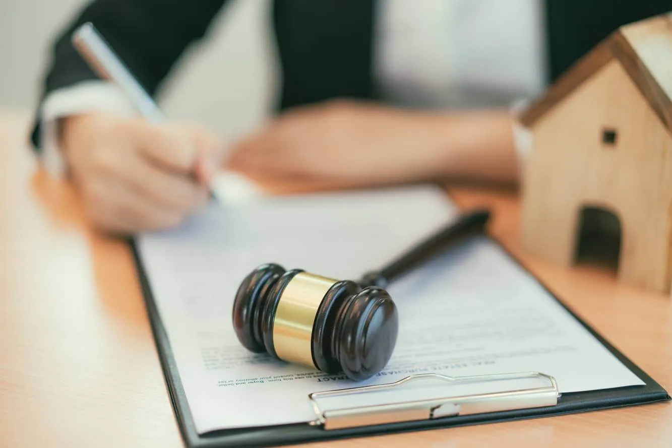 judge's gavel on a legal document next to a wooden house and man signing a lien