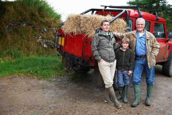 Grandfather, adult son, and grandson standing next to a pickup with hay on the family property
