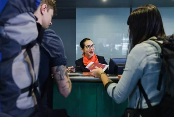 Young couple wearing travel back packs showing their travel documents to an airport checking agent