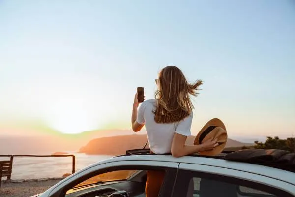 Woman at beach on her spring break trip making a phone video of the sunset as she stands up out of her car sun roof  