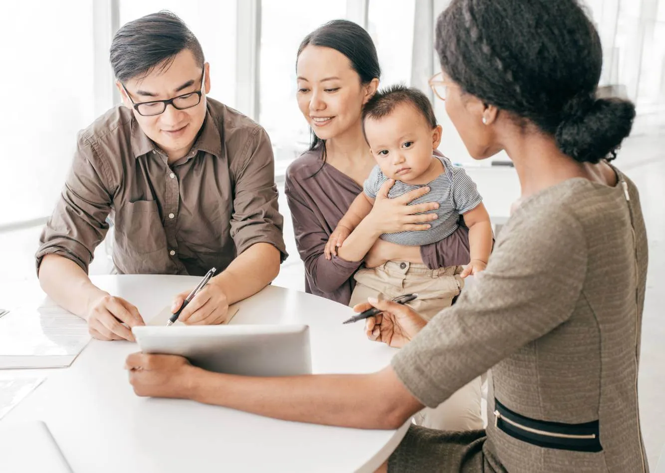 Father signing a Will on a tablet while lawyer, mother and young child look on