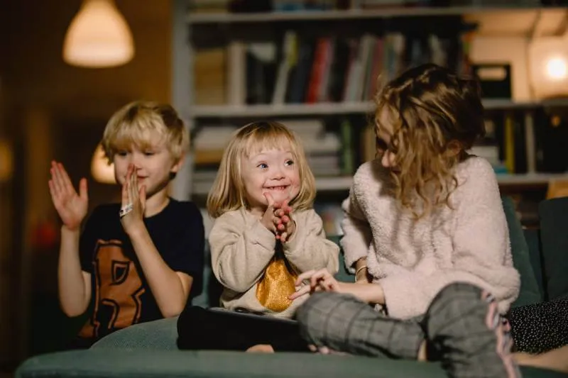 Small girl with Down's Syndrome sitting on a sofa clapping with her brother and older sister