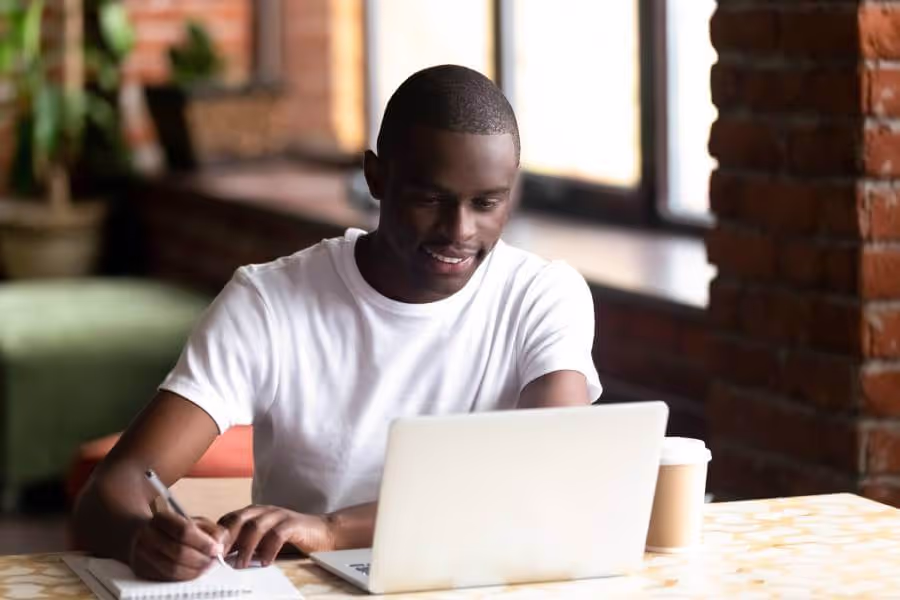 College student studying using his laptop and taking notes