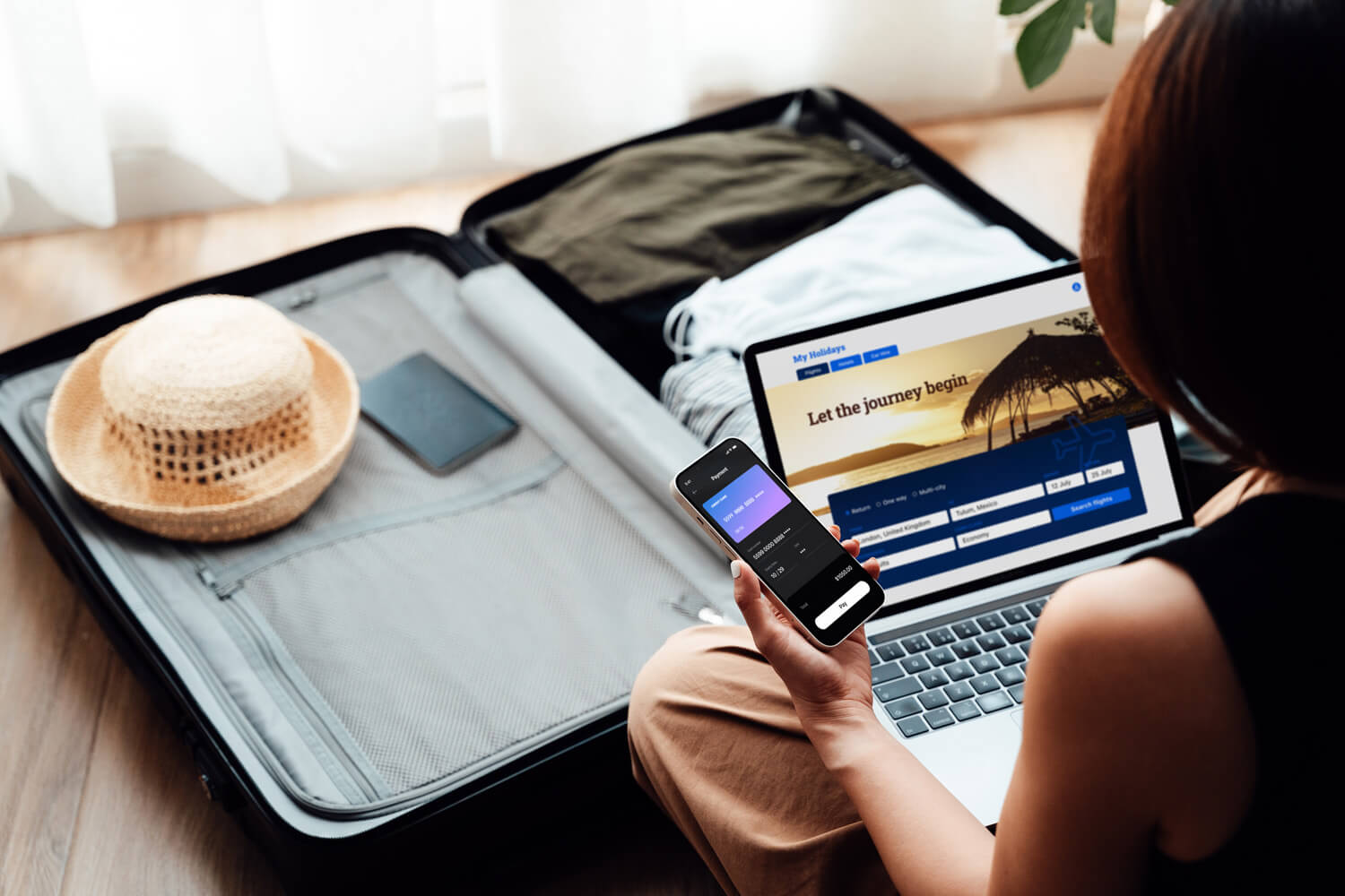 Over the shoulder view of young woman booking a flight via laptop and smartphone