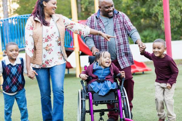 happy family leaving a playground with the 3 children including a girl in a wheelchair