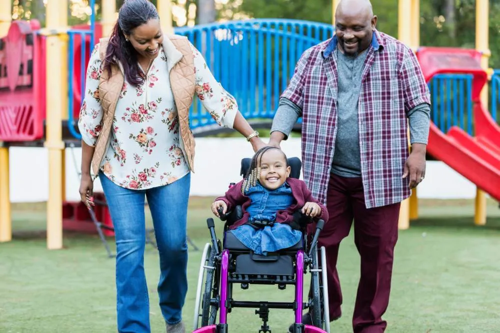 A special needs child in a wheelchair with parents at a playgrounds