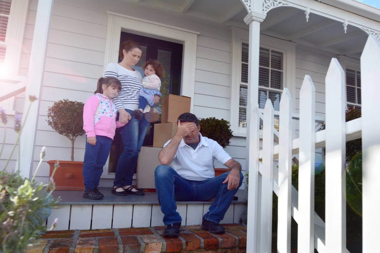 upset homeowner facing foreclosure sitting on porch with his wife, 2 daughters and moving boxes