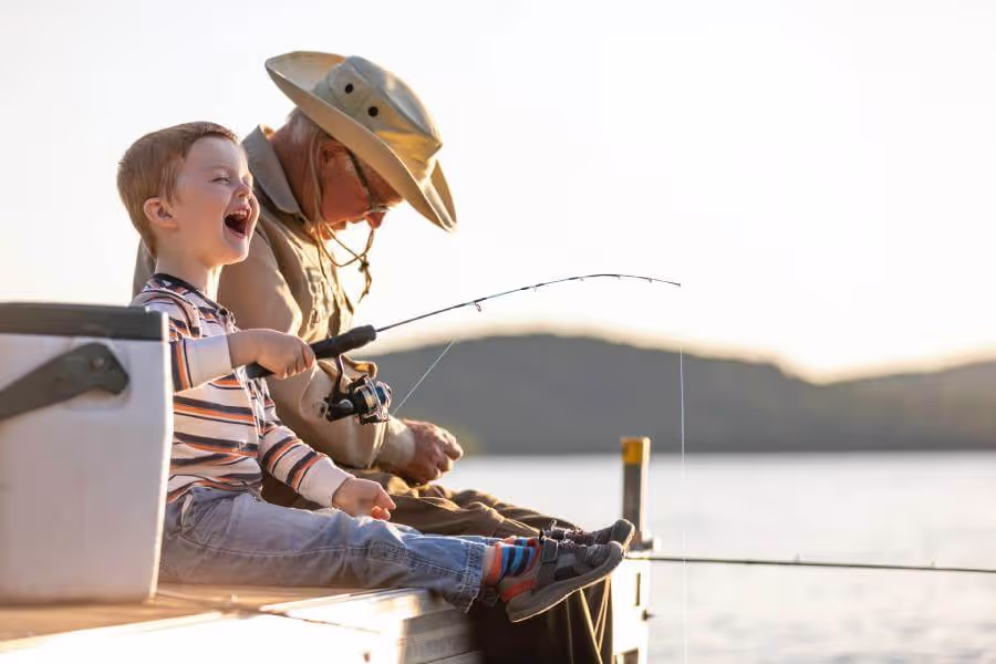 Grandpa and young grandson sitting on lake dock while fishing.