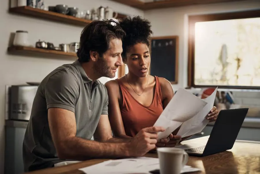 Young couple looking at a Will document in their kitchen|Couple sitting on couch with laptop discussing their Will