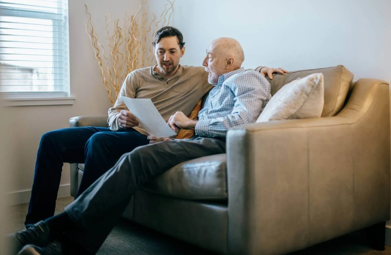elderly man discussing his estate beneficiaries with his son while sed on a living room sofa