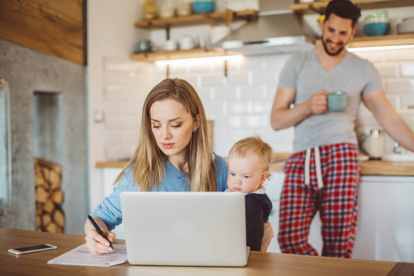 Wife holding a small boy working on her will at kitchen table as husband looks on