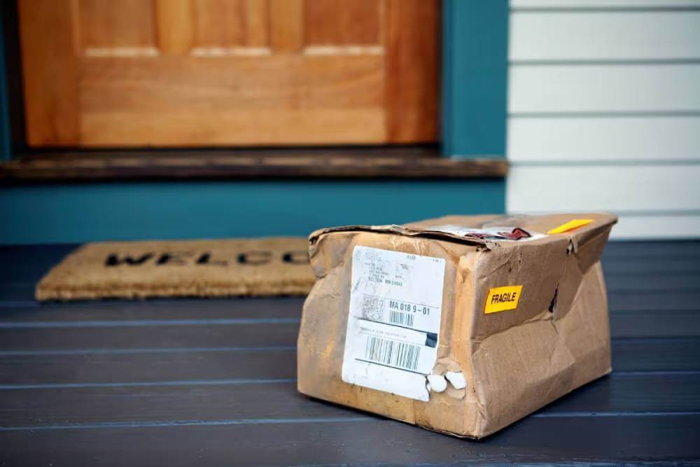 Damaged delivery box marked Fragile on porch near house front door.|Disappointed woman holding a damaged picture frame while talking on the phone and looking at a packing slip.|Frustrated woman talking on phone and looking at a damaged purchase.