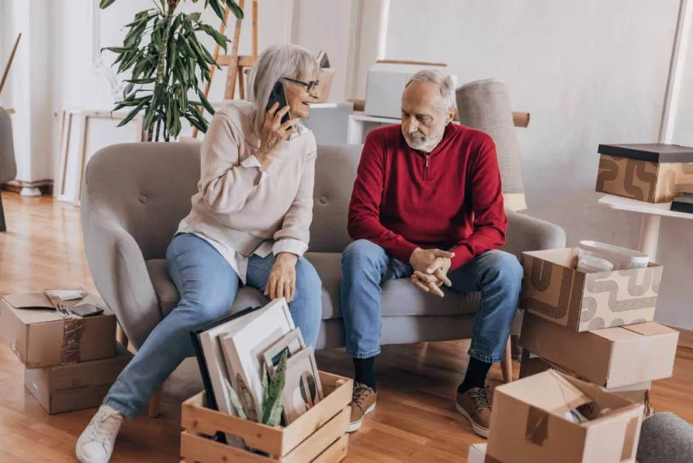 Mature couple in the process of moving. Woman is talking on a smartphone to inquire about moving insurance.