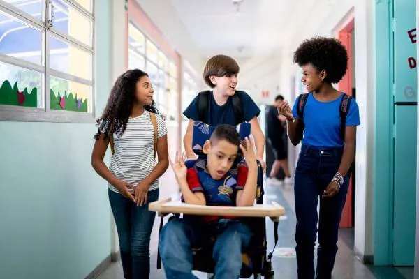 Disabiled student being pushed in a school hallway by 3 friends