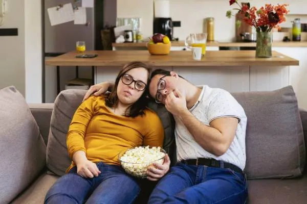 Disabled couple with Down Syndrome on sofa eating popcorn together