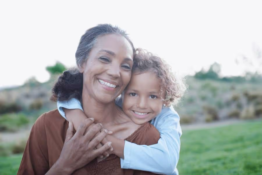Young child hugging older woman who serves as child' guardian|Grandma legal guardian talking to her granddaughter while sitting on sofa