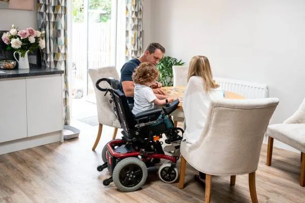 Young disabled boy in a wheelchair sitting at table with his parents in the dining room as they work on a puzzle