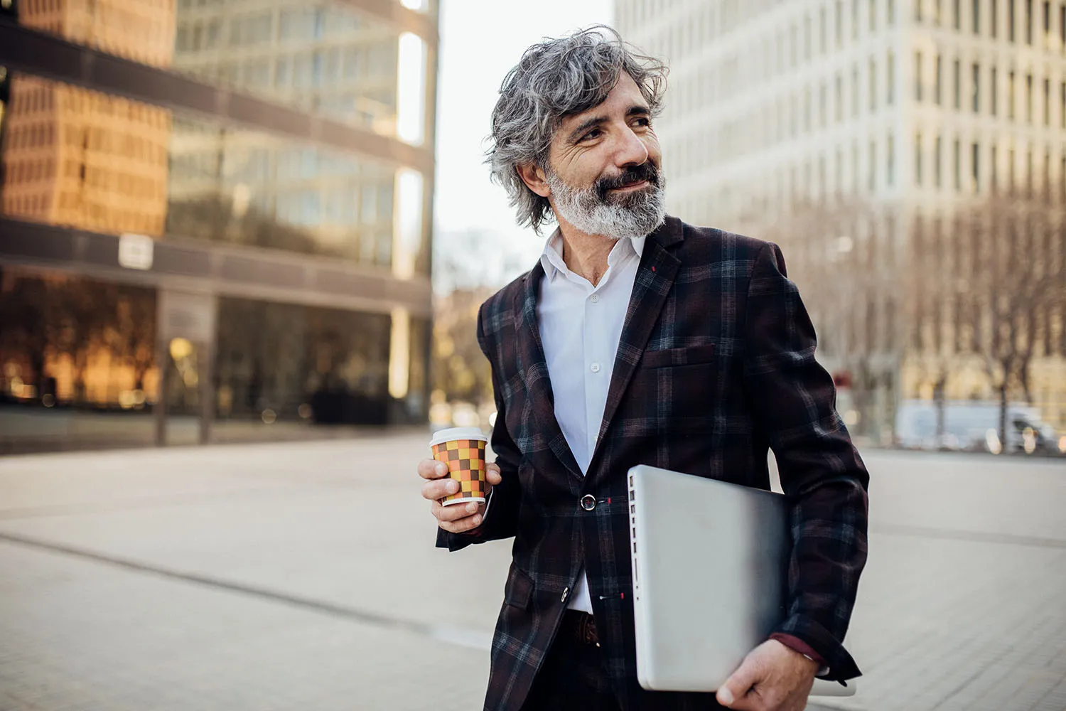 Lawyer walking in city holding coffee and laptop.