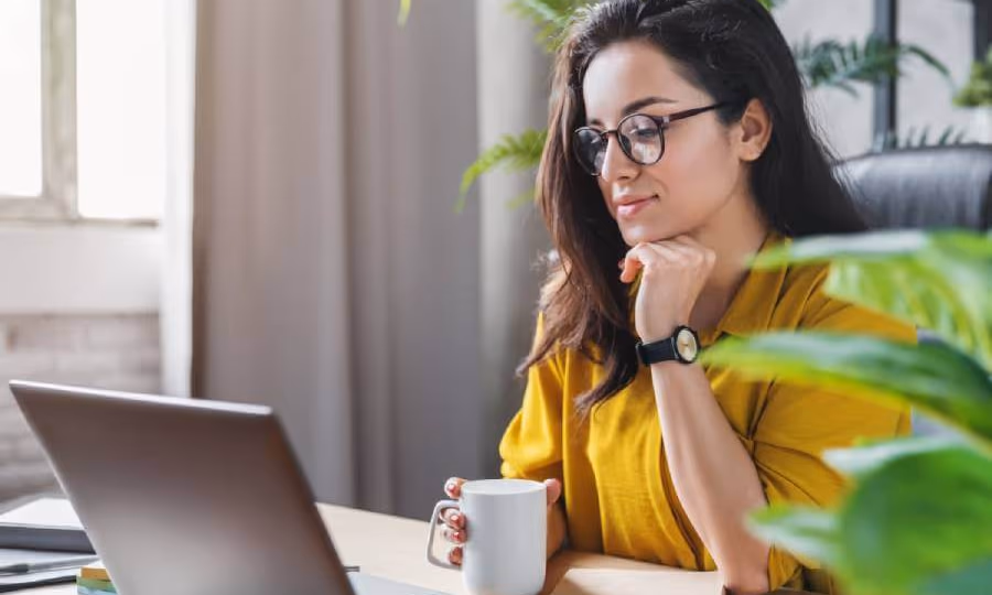Woman looking at laptop and holding a coffee cup while conducting a title search.