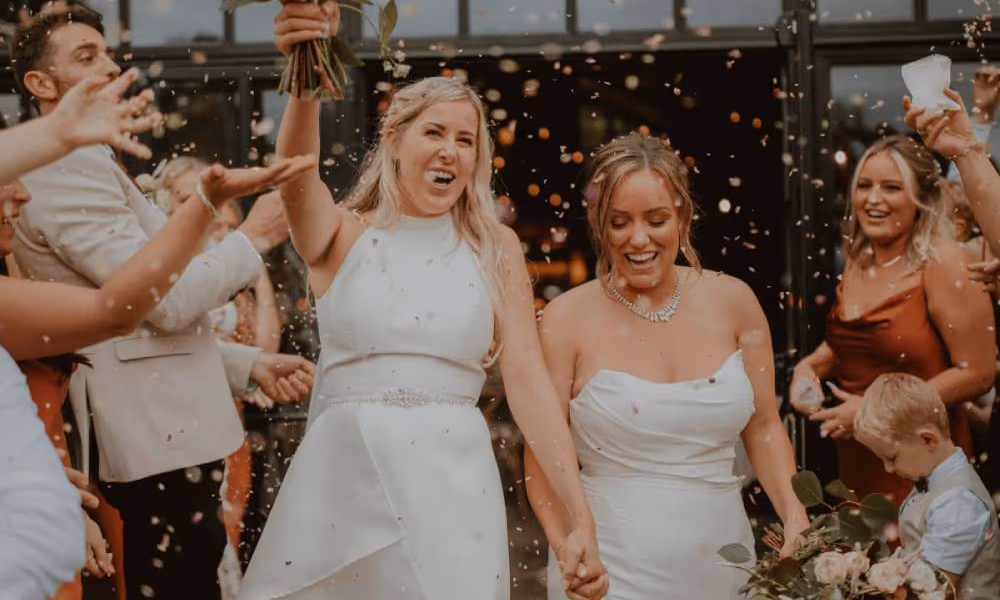 2 brides leaving their marriage ceremony in celebration as confetti is being thrown at them.