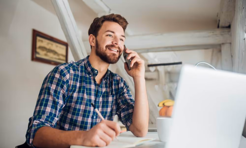 Smiling man working and talking on a cell phone in a casual workspace.