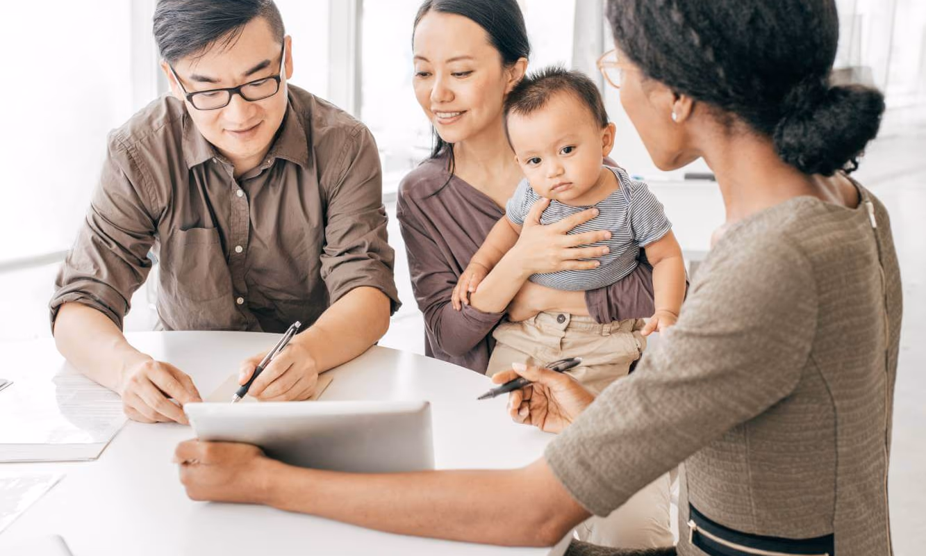 Father signing a Will on a tablet while lawyer, mother and young child look on