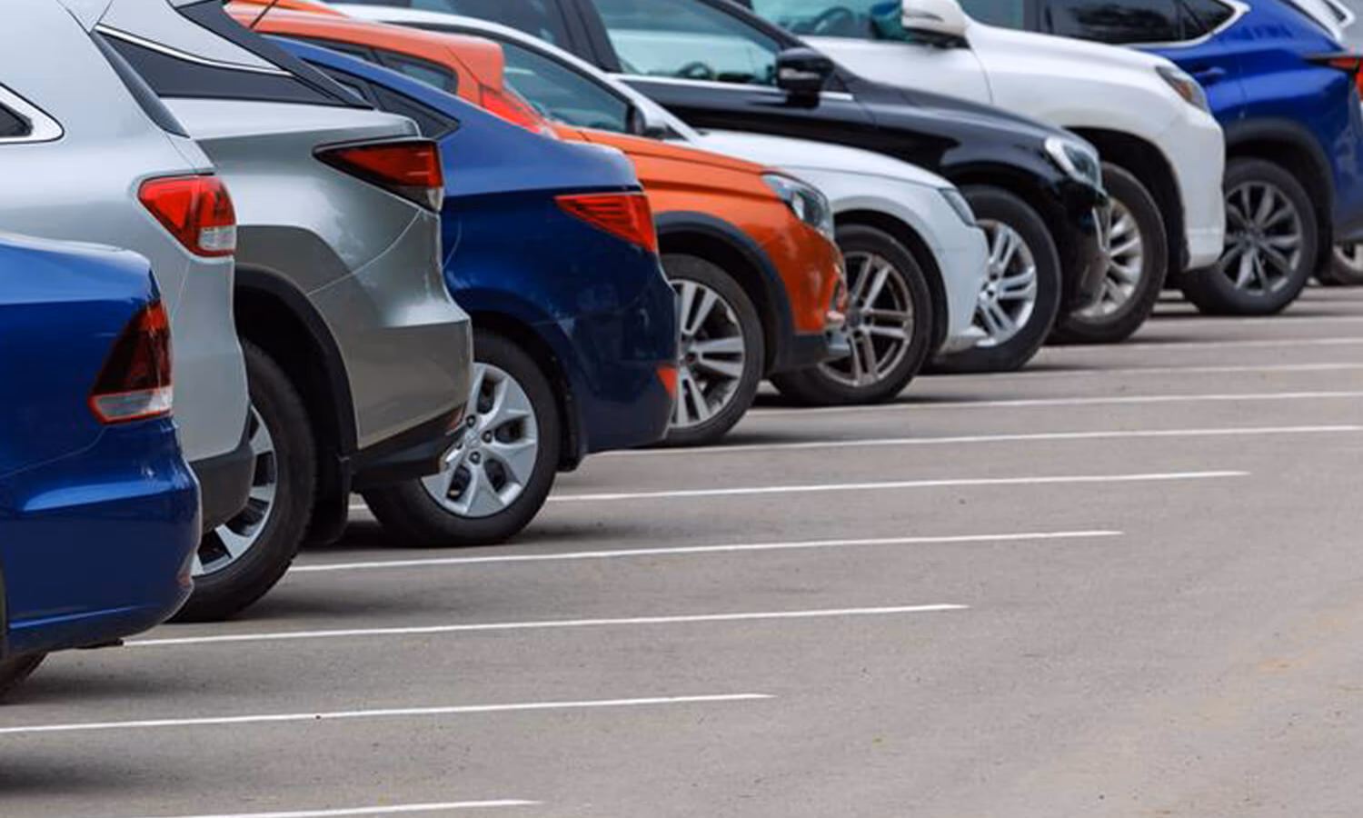Row of different color cars on asphalt parking lot at cloudy summer day