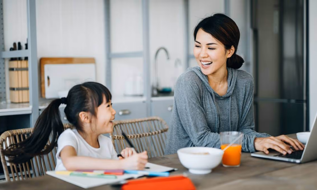Mom typing on laptop and daughter coloring at kitchen table