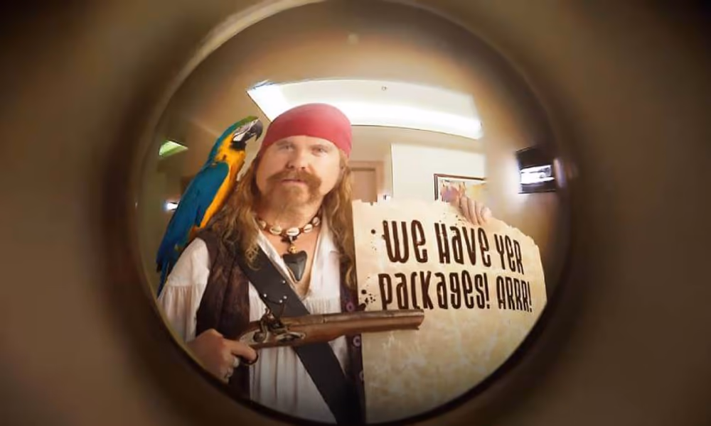 Man dressed as a porch pirate holding a sign that says, We have your packages! Arrr!