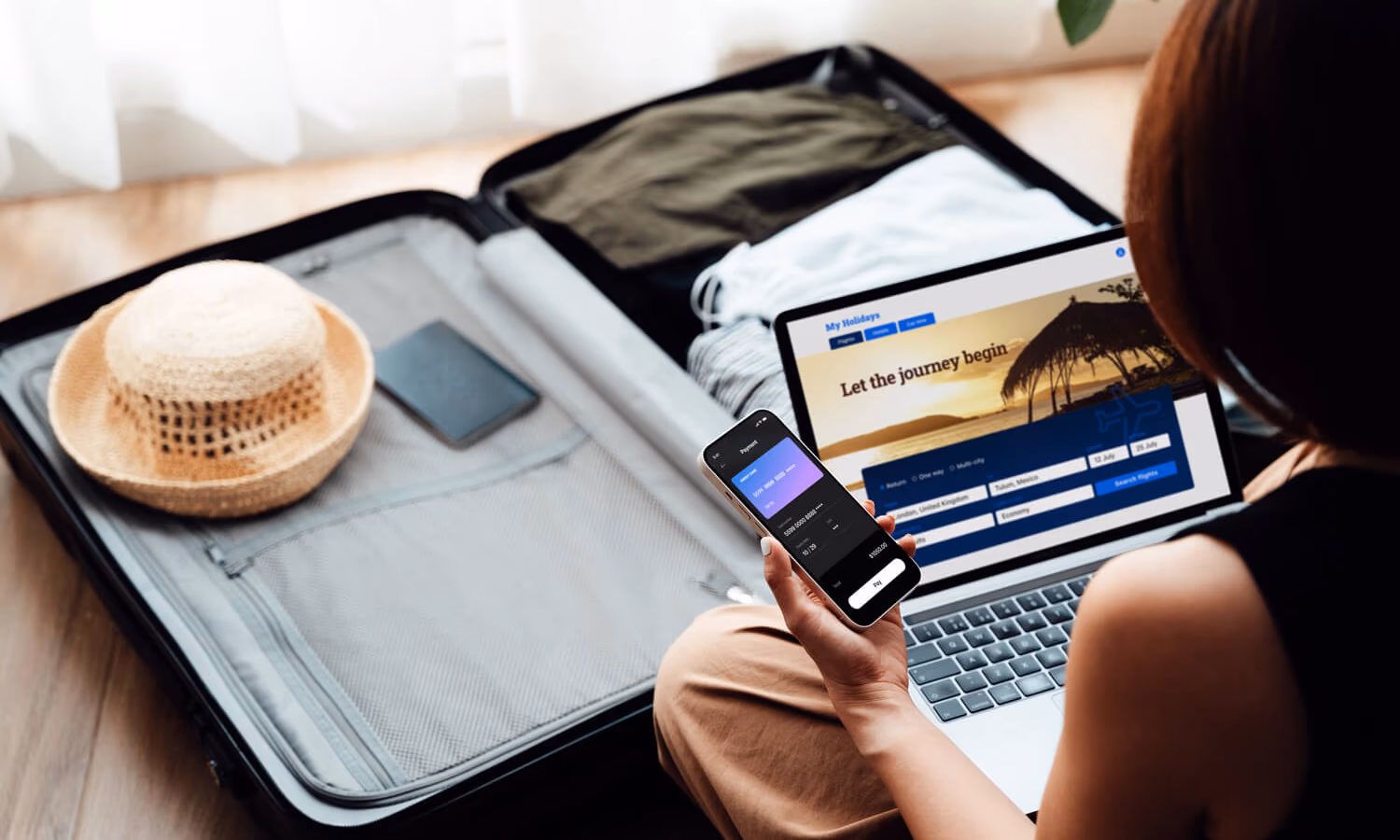 Over the shoulder view of young woman booking a flight via laptop and smartphone