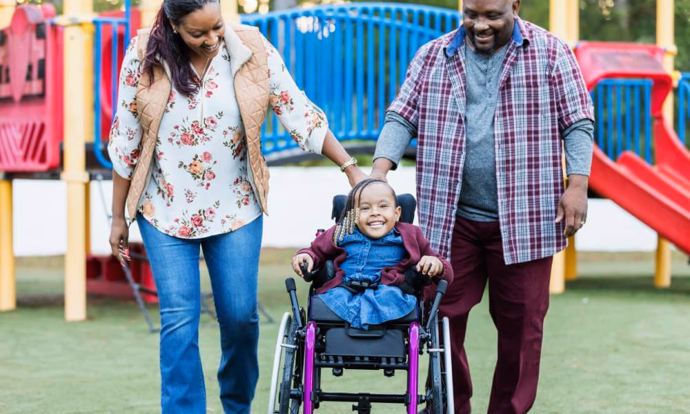 A special needs child in a wheelchair with parents at a playgrounds