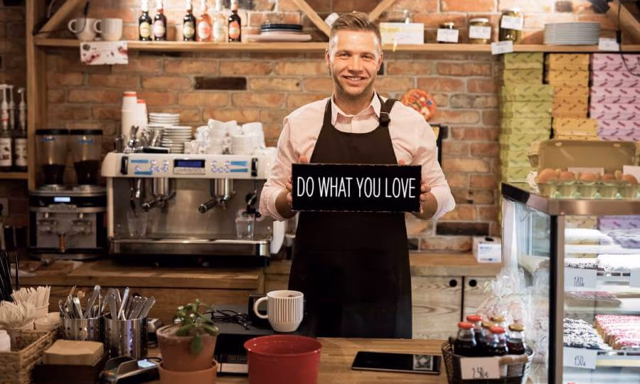 Small business coffee shop owner holding a sign that says, Do What You Love