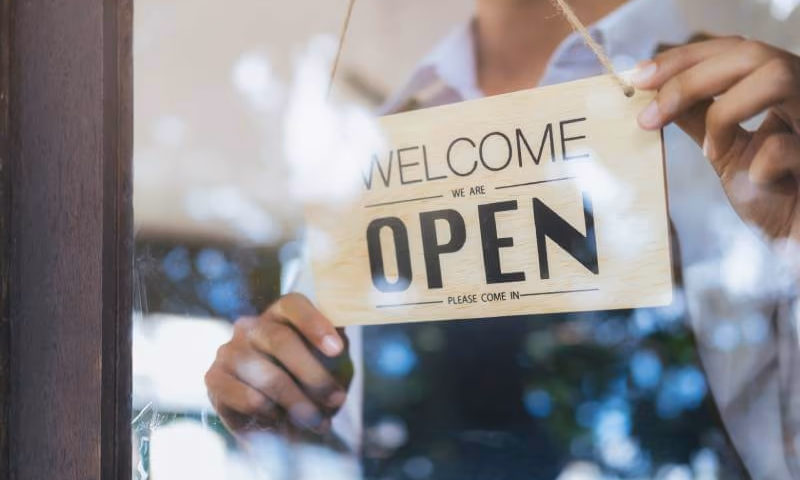 Business owner hanging a welcome we are open please come in sign on business door