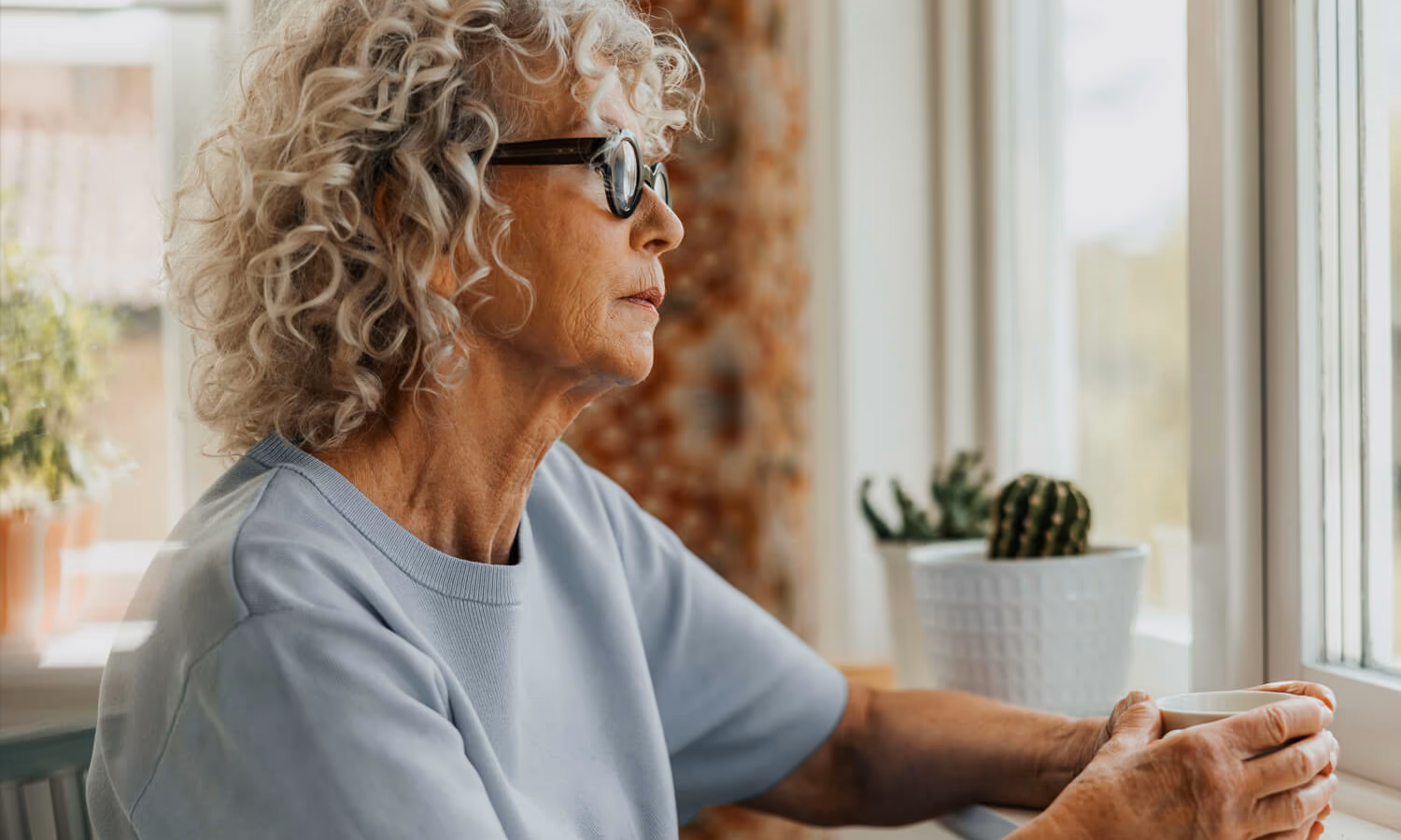 Thoughtful senior woman holding coffee cup while looking through window at home